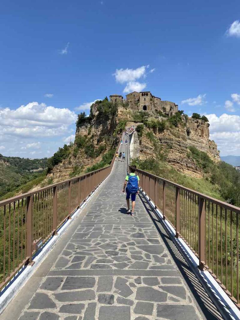 boy walking on the tall bridge leading into Civita di Bagnoregio Italy