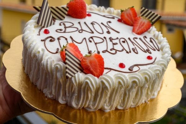 Cream cake with buon compleanno (happy birthday in Italian) written on it in chocolate sauce. 