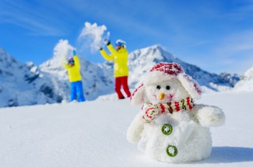 snowman on mountain slope with child and dad playing in the background