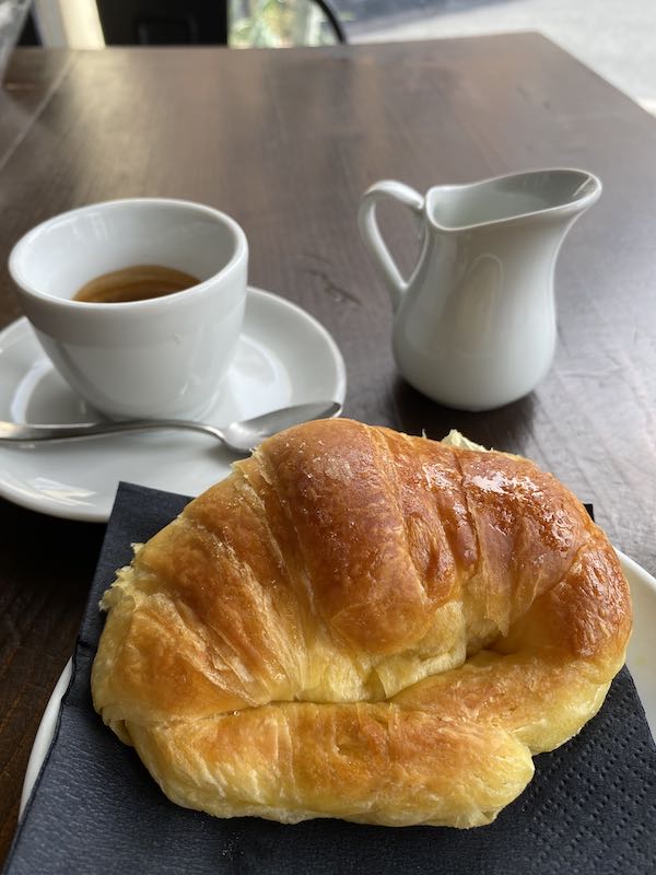 Table with Italian cornetto (pastry), espresso and a small jug of milk.