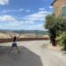 Small girl jumping for joy in Tuscany with rolling hills backdrop and traditional stone house