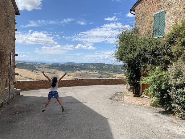 Small girl jumping for joy in Tuscany with rolling hills backdrop and traditional stone house
