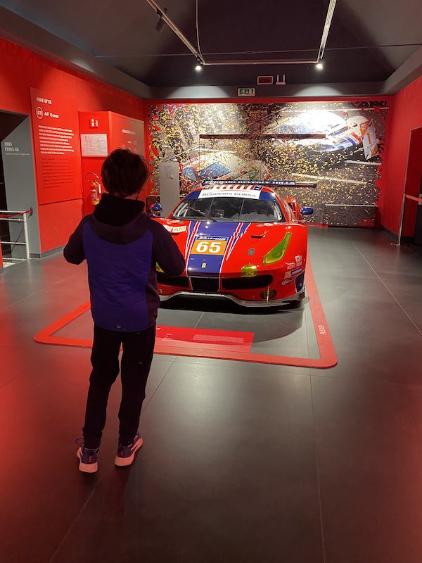child taking photo of a red and blue ferrari car in the Ferrari Museum in Maranello