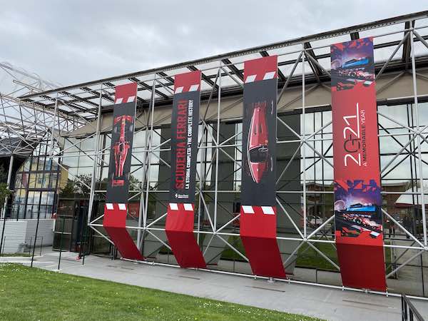 Outside of the main building of the Ferrari Museum in Maranello with vertical red and black banners with photos of Ferrari cars