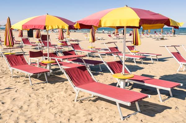 Red and yellow umbrellas and sun loungers in beach club in Italy
