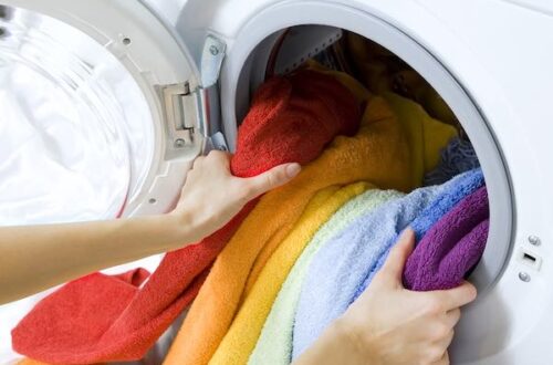 woman hands taking out of washing machine a colorful load of laundry