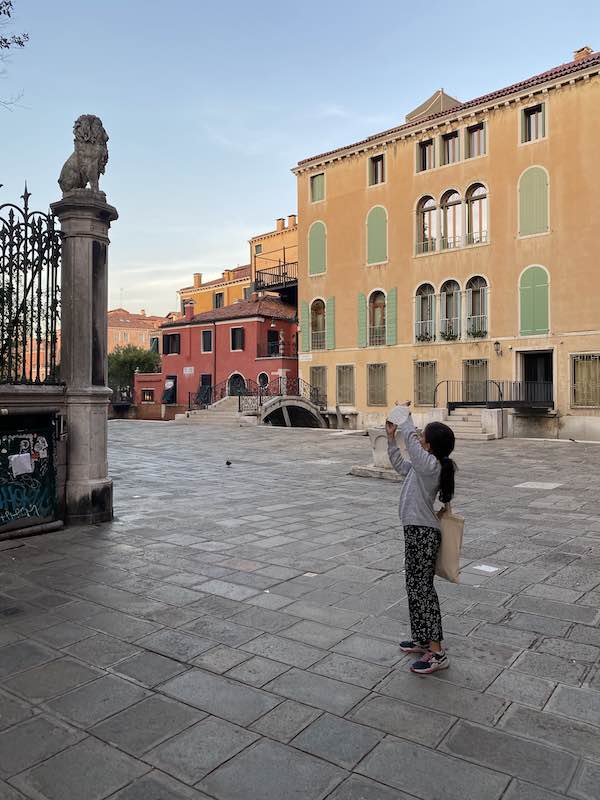 child in Venice Italy taking a photo of a sculpted lion