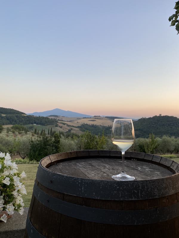 Glass of white wine over barrel with the backdrop of the landscape of Val d'orcia Tuscany 