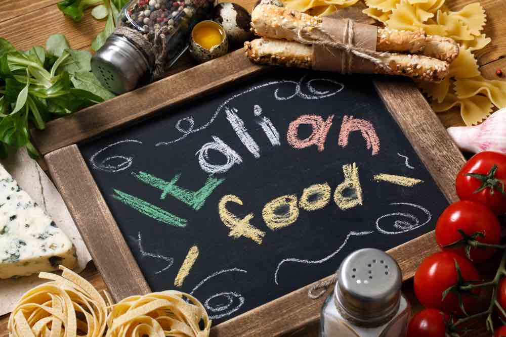 board with "Italian food" written on it and pasta, tomatoes and other Italian ingredients around